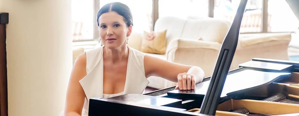 Olga Balakleets Sitting With One Arm On Piano