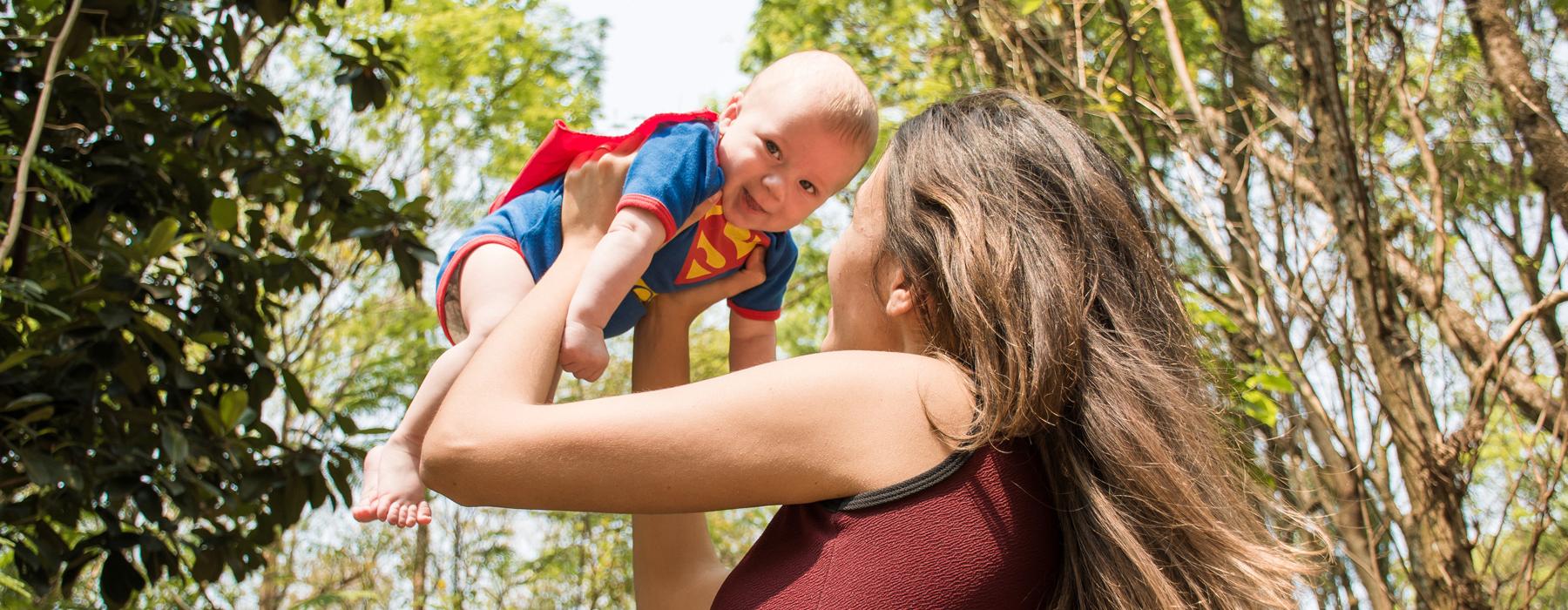 Woman Lifting  In The Air Baby Wearing A Super Man Costume