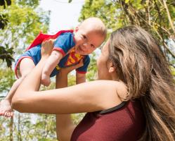 Woman Lifting  In The Air Baby Wearing A Super Man Costume