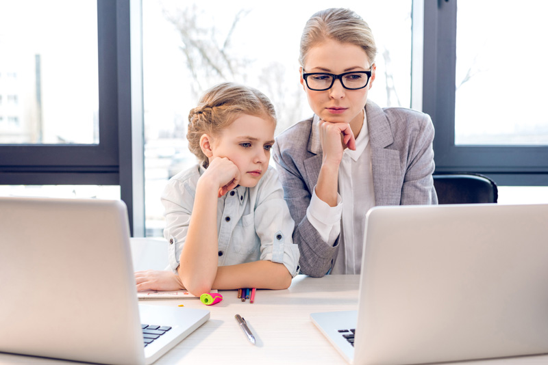 Mother And Daughter In Business Suits Concentrating And Looking At Laptop 