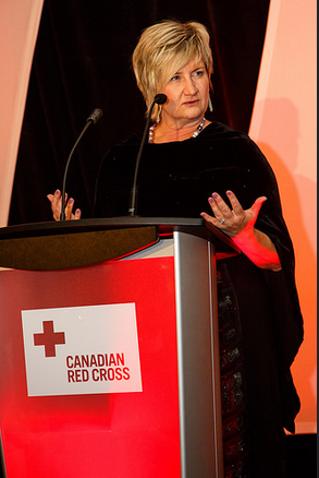 Kelly Garrett Speaking At Podium With Canadian Red Cross Sign