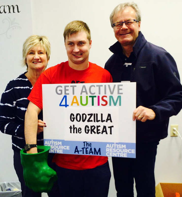 Kelly Garrett And Her Husband Supporting Their Son Connor Holding Sign Godzilla the Great In Raising Money Autism Resource Centre