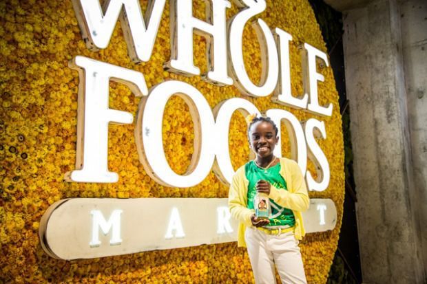 Mikaila Ulmer Smiling And Standing In Front Of Whole Food Sign Holding Bottle of Lemonade