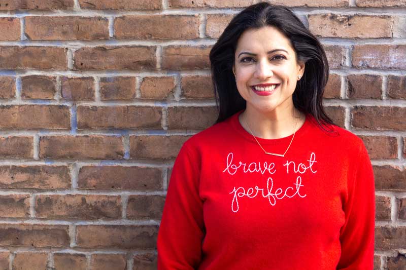 Reshma Saujani Against Brick Wall Wearing Red Shirt With Brave Not Perfect Written On It 