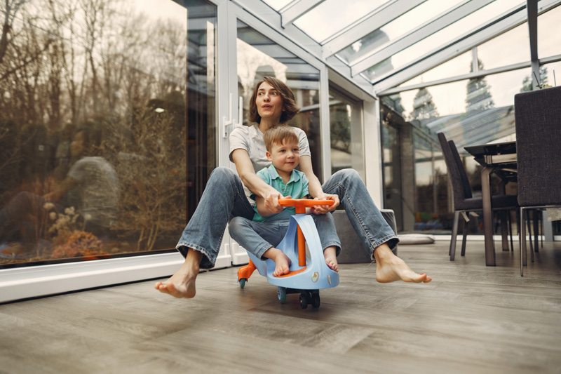 Mother And Son Riding Kids Scooter In Kitchen