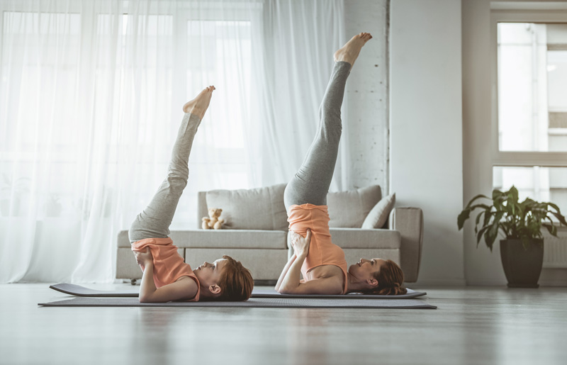 Mother And Daughter Doing Yoga In Living Room